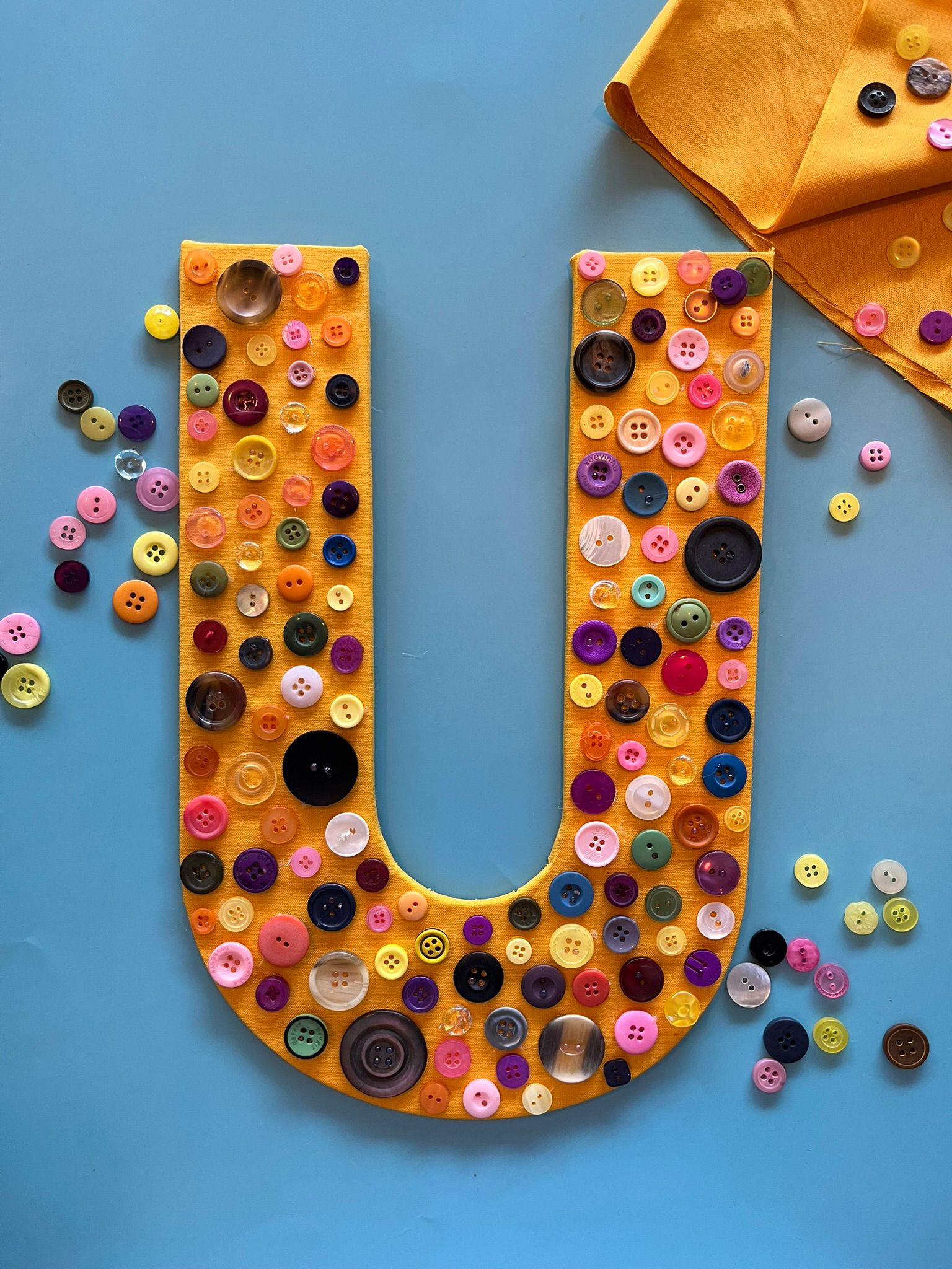 Buchstabe U beklebt mit bunten Knöpfen